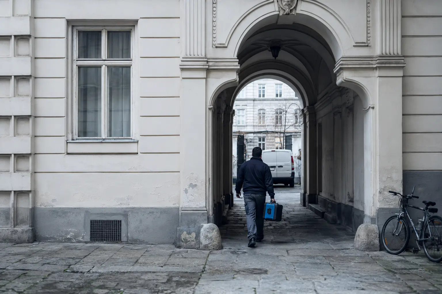 Techniker mit Werkzeugkoffer im Durchgang eines Wiener Hofs